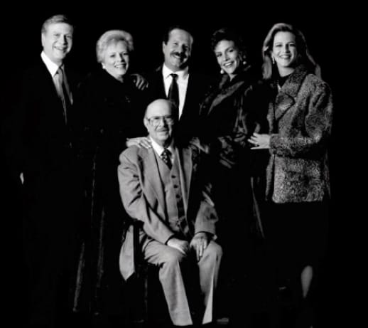 Black and white portrait of the smiling Stupp family: six members (three men, three women) in formal attire, one man seated.